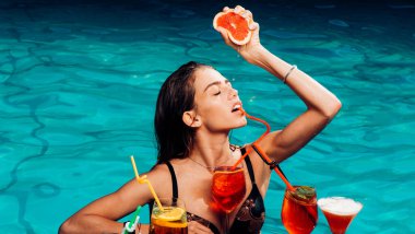 Yaz kadını turuncu sıkar. Yaz havuzunda güzellik kraliçesi. Havuz başında bikinili bir kadın. Tropik yaz cenneti. Yaz tatili. Kokteyl partisi. Seksi model içki kokteyli.