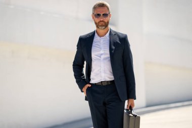 Açık hava iş portresi. Dışarıda yürüyen bir iş adamı. Şirket lideri harekete geçti. Çantalı takım elbiseli adam. İşadamı işe gidiyor. Çantası olan bir iş adamı. İşadamı ofise git.
