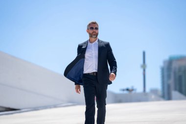 Dışarıda yürüyen bir iş adamı. Takım elbiseli başarılı bir iş adamı, tam vücut. Takım elbiseli kendine güvenen bir iş adamı. İşadamı çekip gidiyor. Zarif takım elbiseli zengin adam. Kendine güvenen şehirli iş adamı.