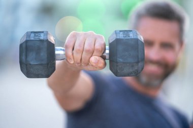 Olgun bir adamın dambılları dışarı kaldırırken yakın çekimi. Olgun adamların kol kasları halter egzersizi yapıyor. Kol halterine yakın çekim. Dambılı formda bir erkek kolunun yakın çekimi.