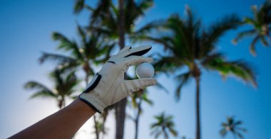 Golf topu ve mavi gökyüzü yaz palmiyesi. Elle tutulan golf topu. Yaz golf sahası. Golf sahasında palmiye ağaçları. Eldiven takan golfçü. Yazın oynuyorum. Golf kulübü afişi.