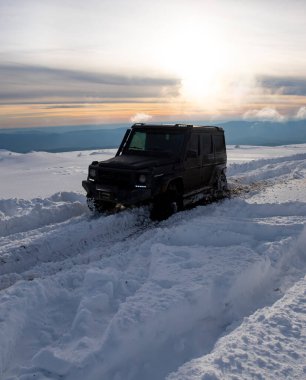 01.02.2021, Karpatlar. Gün batımında kar içinde off-road SUV. 4x4 jipli bir kış seferi. Kış doğasında zorlu bir off-road gezisi. Off-road arabalı dağ yolu. Kar yolunda macera gezisi