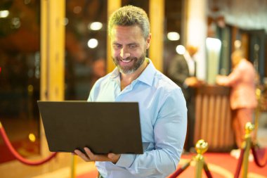 Gece sokakta dizüstü bilgisayar kullanan bir iş adamı. İş adamı dışarıda dizüstü bilgisayarda çalışmayı planlıyor. İşadamı, neon şehir ışıkları altında dizüstü bilgisayarda geziniyor. Serbest çalışan bir iş adamı. Gece işi.