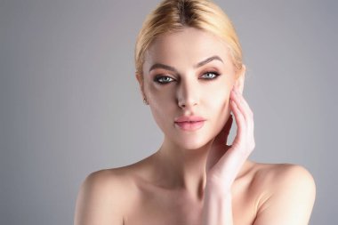 Beautiful tender woman posing in studio. Cosmetics. Sensual woman with bare shoulders posing sensually. Young sensual woman with nude make-up on studio background. Perfect skin, beauty face