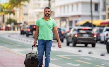 Bavullu bir turist sokaklarda yürüyor. Bir erkek turist, tropikal bir şehirde yaz tatilinin tadını çıkarır. Bavullu bir turist şehir manzarasını keşfediyor. Erkek turist şehirde yürüyor