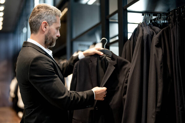 Модный костюм. Латиноамериканский бизнесмен ценит хороший пошив и костюм. Хорошо одетый мужчина позирует в бутике костюмов. Помощник продавца помогает стильному человеку найти идеальный костюм