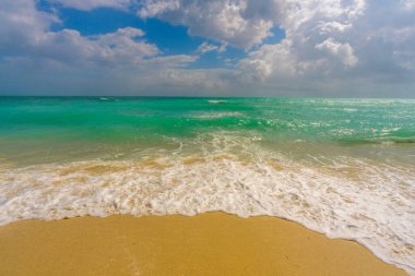 Turkuaz su dalgası hareketi. Yaz plajı. Sakin plaj. Lüks sahil beldesi. Parlak gökyüzü ve sahilde dalgalar. Güzel köpüklü kıyı şeridi. Deniz arka planı. Mavi okyanus. Kumsal. Dramatik fırtına dalgaları