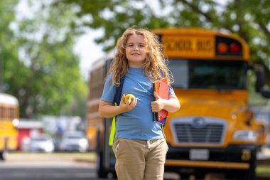 Okul otobüsü dışarıda çocuk öğrenciyi bekliyor. Sırt çantalı sarışın çocuk ve okula gitmek için not defterleri. Devlet okuluna kadar yürüdüm. Amerikan okulunda eğitim, öğrenim ve bilgi kavramı