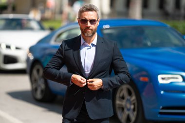 Olgun bir iş adamı. Lüks bir arabanın yanında duran zengin bir işadamı. Küresel. Endüstri lideri. Başarılı bir iş. Pahalı bir arabanın önünde duran şık, lüks bir iş adamı.