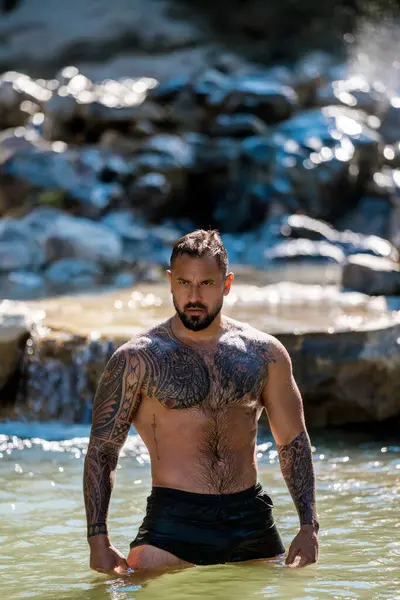 Kaslı erkek güzelliği. Su damlalı kaslı gövde. Doğadaki kaslı adam. Sağlıklı yaşam tarzı ve enerji. Çıplak göğüs. Doğadaki zindelik. Su sıçratarak kas çalışan bir adam.