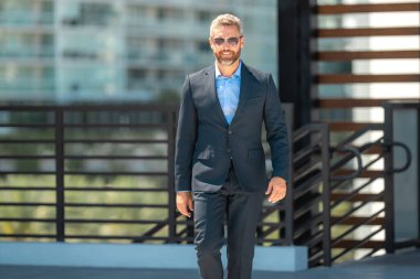 Başarılı bir iş adamı dışarıda yürüyor. Kendine güvenen bir iş adamı. Başarı işi. Takım elbiseli olgun iş adamı. Yakışıklı şirket lideri. Şehir ortamında zengin bir iş adamı. Zarif iş lideri.