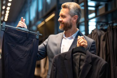 Bir adam butikte alışveriş yaparken klasik bir terzi kıyafeti giyer. Başarılı bir iş adamı için klasik bir kıyafet. Takım elbiseli modaya uygun bir mağaza. Takım elbise seçen bir iş adamı. Bir erkek resmi etkinlik için takım elbise seçer.