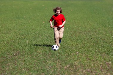 Parkta bir çocuk futbol oynuyor. Bir çocuk futbol topunu tekmeliyor. Çocuklar spor yapıyor. Çocuk futbolcu kaleye doğru koşuyor. Çocuk futbol topunu tekmeliyor. Sportif bir çocuk. Çocuklar sahada futbol oynuyor.
