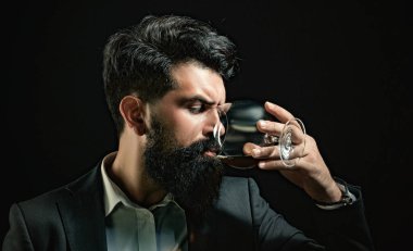 Sakallı adamın tuttuğu konyak bardağı. Barda yalnız başına konyak içen adam. Klasik bardakta viski konyağı. Konyak retro tarzında tatmak. Pahalı viski. Viski konsepti iç. Alkolik içecek.