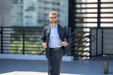 Başarılı bir iş adamı dışarıda yürüyor. Kendine güvenen bir iş adamı. Başarı işi. Takım elbiseli olgun iş adamı. Yakışıklı şirket lideri. Şehir ortamında zengin bir iş adamı. Şık bir iş ve lider.