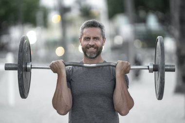 40 'lı yaşlardaki adam spor yapıyor. Sağlıklı egzersiz. Halterli Miami plajı fitness modeli. Sağlıklı yaşam halter eğitimi. Olgun bir adam halterle dışarıda egzersiz yapıyor. Halter kaldıran adam.