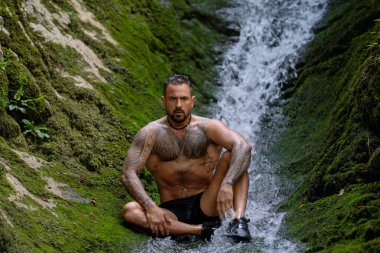 Kaslı erkek güzelliği. Su damlalı kaslı gövde. Doğadaki kaslı adam. Sağlıklı yaşam tarzı ve enerji. Çıplak göğüs. Doğadaki zindelik. Su sıçratarak kas çalışan bir adam.