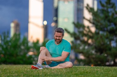 Koştuktan sonra diz ağrısı. Dizinden yaralanan bir adam. Egzersiz bacak ağrısına neden oluyor. Koşu diz travmasına yol açıyor. Açık hava egzersizi ve diz incinmesi. Şehir parkında koşudan kaynaklanan sağlık sorunları. Bacağım acıyor.