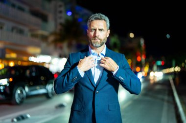 Gece vakti poz veren başarılı bir iş adamı. Gece sokağında takım elbiseli zengin bir adam duruyor. Resmi takım elbiseli yakışıklı bir iş adamı. Şık bir iş adamı. Zarif bir iş adamı. Zengin iş adamı.