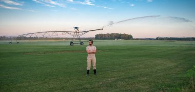 Bir çiftçi sulama çiftliğini suluyor. Adam su tarlası için sulama yapıyor. Sulama alanındaki çiftçi çimlerin üzerine su serper. Çiftlikte sulama sistemi devrede. Sulama alanı için sprey