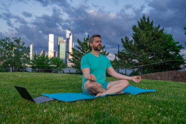 Latin Adam dışarıda otların içinde meditasyon yapıyor. Sporcu şehir parkında yoga yaparken asana meditasyonu yapıyor. Atletik erkek meditasyonu, rahatlama, sağlıklı yaşam tarzı kavramı. Açık havada meditasyon.