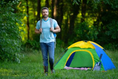 Doğada sırt çantasıyla dolaşan bir gezgin. Doğaya yaz gezisi. Orman kampında dinlenen adam. Kamp gezisi. Yürüyüşten sonra çadırın yanında dinleniyor. Barışçıl bir kamp alanında özgürlük tatili. Piknikteki Adam
