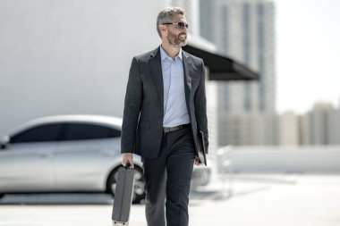 Başarılı bir iş adamı evrak çantasıyla dışarıda dolaşır. İş adamı evrak çantasını dışarıda tutuyor. Takım elbiseli olgun iş adamı. Şirket işi. Takım elbiseli zengin iş adamı. Açık hava iş portresi