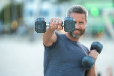Dambıllar kol kola. Yetişkin bir adamın dambılları dışarı kaldırması. Kol kasları dambıl egzersizi yapıyor. Kol halteri tutun. Dambılı bir erkek kolunun yakın çekimi.