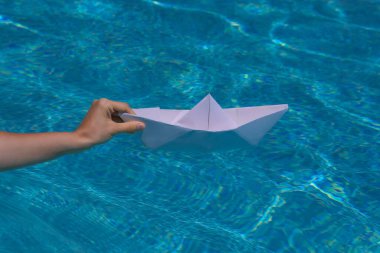 Suda yüzen kağıttan tekne dalgalara ve dalgalara neden olur. Kağıttan bir tekneyi suya batırmak.