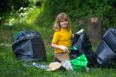 Lastik eldivenli çocuk çöp torbasıyla ormandaki çöpleri temizliyor. Eko, çevre koruma. Kirliliği geri dönüştür. Çocuk çöp ve plastik çöp topluyor. Ortamı kaydet
