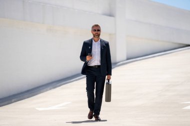 İş portresi. Dışarıdaki telefondan iş adamı aradı. Başarılı lider hareket halinde. Takım elbiseli, çantalı bir adam telefonda konuşuyor. İşadamı işe gidiyor. Çantası olan bir iş adamı. İş başarısı