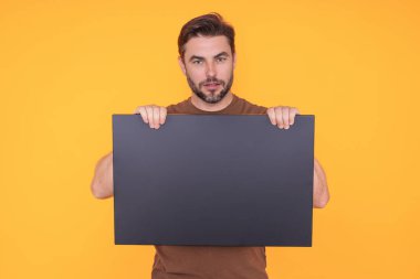 Tabela yakışıklı adamda, boş kart. Ürününüz için pankart hazır. Stüdyonun izole edilmiş arka planında boş tabela gösteren bir adam portresi. Boş tahta var. Reklamcılık ve kopyalama alanı kavramı