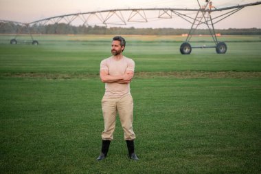Bir çiftçi sulama çiftliğini suluyor. Adam su tarlası için sulama yapıyor. Sulama alanındaki çiftçi çimlerin üzerine su serper. Çiftlikte sulama sistemi devrede. Sulama alanı için sprey