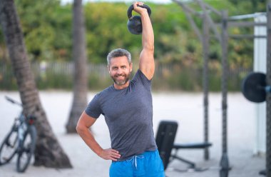 Kettlebell dışarıda çalışıyor. Atletik adam kettlebell kaldırıyor. Kettlebell 'le antrenman yapan zinde bir adam. Gömleksiz sporcu kettlebell egzersizleri yapıyor. Olgun adam dışarıda antrenman yapıyor. Açık havada antrenman yapmak