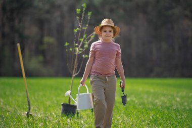 Çocuk kürekle ağaç dikiyor. Çocuk arka bahçeye ağaç dikiyor. Bahar tarlasında ağaç diken çocuk. Sulama kovası ve kürekle ekmek. Bahçe çiftliğinde ağaç yetiştiren çocuk. Çocuklar çalışır.