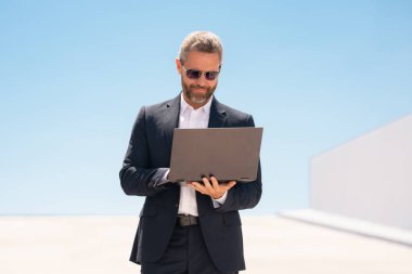 İş adamı dışarıda dizüstü bilgisayar kullanıyor. Dizüstü bilgisayar kullanan 40 'lı yaşlarda biri. Dizüstü bilgisayarı olan kendine güvenen bir iş adamı. İnternette iş. İş adamı laptoptaki verileri kontrol ediyor. Takım elbiseli iş adamı internette çalışıyor.