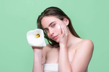 Stüdyo arka planına izole edilmiş yüz kremi süren güzel, yarı çıplak bir kadının portresi. Cilt bakım ürünü. Yüzünde nemlendirici krem var. Mükemmel cilt, sabah rutini