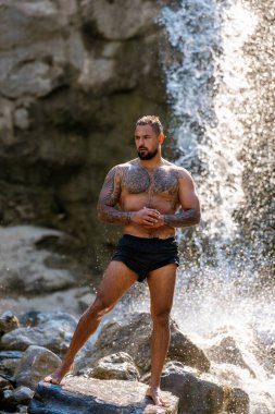 Kaslı erkek güzelliği. Su damlalı kaslı gövde. Doğadaki kaslı adam. Sağlıklı yaşam tarzı ve enerji. Çıplak göğüs. Doğadaki zindelik. Su sıçratarak kas çalışan bir adam.