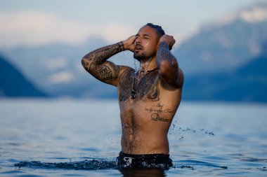 Seksi yaz erkeği. Suda ıslak kaslı erkek vücudu. Çıplak seksi erkek vücudu. İnsan yaz doğasında suya su sıçratır. Yaz plajında poz veren formda bir adam. Dağ gölünde su sıçratan güçlü bir adam. Yaz gezisi