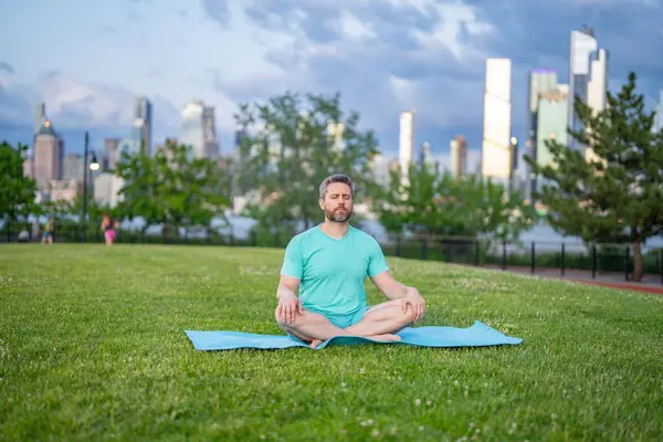 Nilüfer çiçeği içinde meditasyon yapan bir adam dışarıda çimlerde poz verir. Sporcu şehir parkında yoga yaparken asana meditasyonu yapıyor. Atletik erkek meditasyonu, rahatlama, aktif sağlıklı yaşam tarzı kavramı. Açık havada meditasyon.