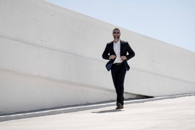 Dışarıda yürüyen bir iş adamı. Takım elbiseli başarılı bir iş adamı, tam boy. Takım elbiseli kendine güvenen bir iş adamı. İşadamı çekip gidiyor. Zarif takım elbiseli zengin adam. Kendine güvenen şehirli iş adamı.