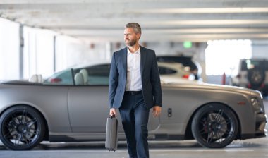 Lüks bir arabanın yanında zengin bir işadamı. Takım elbiseli zengin bir iş adamı. Şehirdeki başarılı zengin iş adamı. Kendine güvenen bir iş adamı. Başarı işi. İş adamı sokakta yürüyor