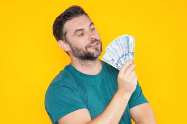 Yakışıklı adam gri stüdyoda izole edilmiş para tutuyor. Dolar banknotları halinde para. Yığınla para, finans, yatırım ve tasarruf