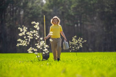 Çocuk bahçeye bir ağaç dikti. Çocuk kürek ve bitki ağacıyla toprak kazıyor. Çocuk bahçıvan meyve ağaçlarıyla ilgileniyor. Çocuklarla ağaç dikmek. Yeşil için çocuk bitkisi. Çocuklar için bahçe işleri. Çocukluk gelişimi