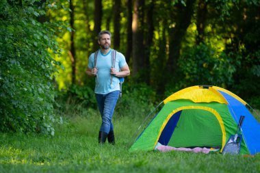 Gezgin doğada kamp yapmaktan hoşlanıyor. Doğaya yaz gezisi. Orman kampında dinlenen adam. Kamp gezisi. Yürüyüşten sonra çadırın yanında dinleniyor. Barışçıl bir kamp alanında özgürlük tatili. Yazın piknikteki adam