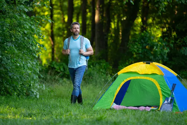 Gezgin doğada kamp yapmaktan hoşlanıyor. Doğaya yaz gezisi. Orman kampında dinlenen adam. Kamp gezisi. Yürüyüşten sonra çadırın yanında dinleniyor. Barışçıl bir kamp alanında özgürlük tatili. Yazın piknikteki adam