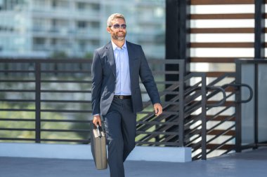 Başarılı bir iş adamı bir evrak çantasıyla dışarıda yürüyor. İş adamı hareket halinde. Takım elbiseli olgun bir avukat. Çantası olan zengin bir iş adamı. Orta yaşlı iş adamı işe gidiyor. Yakışıklı avukat.