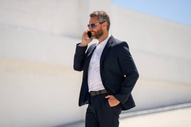 Ofis çalışanı dışarıda cep telefonuyla konuşuyor. Cep telefonunda iş adamı konuşması. İş adamı telefon görüşmesi yapıyor. Şık bir iş adamı telefon kullanıyor. İş görüşmesi. Meşgul işadamı telefonda konuşuyor.