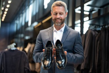Moda mağazasındaki bir müşteri farklı ayakkabı stillerini değerlendirir. İş adamı kendine güvenerek ayakkabıcıdan şık ayakkabılar seçer. Resmi görünmek için klasik deri ayakkabılar. Resmi ayakkabılar. Deri ayakkabılar.