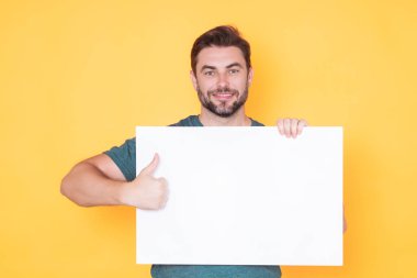 Stüdyonun arka planında boş tahta tutan adam. Kopyalama alanı olan boş tabela gösteren baş parmağı havada bir erkek model. Fikir ve teklif. Reklamınız. Metin, model için boş alanı olan boş tahta reklamı